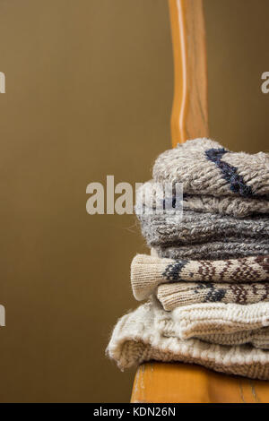 Stack of Handmade Warm Knitted Socks Scarfs Mittens Sweaters From Rough Wool Yarn Brown Beige Grey on Vintage Chair Golden Olive Color Wall Background Stock Photo