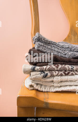Stack of Handmade Warm Knitted Socks Scarfs Mittens Sweaters From Rough Wool Yarn Brown Beige Grey on Vintage Chair Trendy Peach Color Wall Background Stock Photo