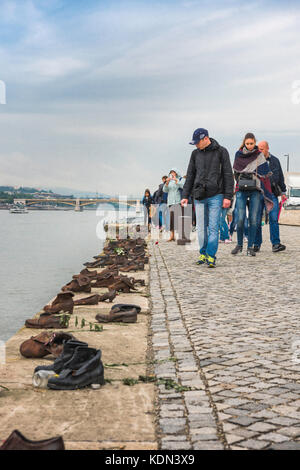 Budapest Holocaust Memorial, tourists view a line of empty shoes alongside the River Danube signifying the city's victims of genocide in the 1940s. Stock Photo