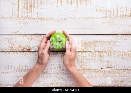 Young Woman Hands Holding Ripe Green Apple on White Plank Wood Background Tabletop. Flat Lay Top View Thanksgiving Harvest Autumn Fall. Gratefulness.  Stock Photo