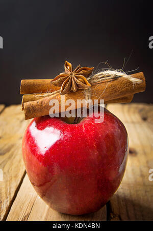 Red Glossy Apple Cinnamon Sticks Tied with Twine Anise Star on Wood Background. Vintage Rustic Style. Christmas New Year Symbol. Greeting Card Poster  Stock Photo