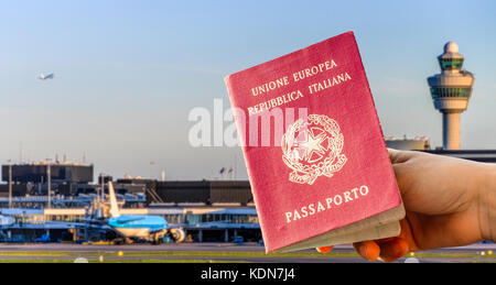 Digital composite of hand holding an Italian passport with busy airport terminal in blurred background Stock Photo