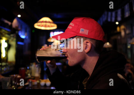 A young Israeli man drinking beer in a pub in Jerusalem and wearing the 'Make America Great Again' classic rope hat that Donald Trump used to wear during his campaign for presidency in the US. Stock Photo