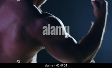 Fighter silhouette. Handsome athletic man in boxing stand on a dark background. Muscular young man in boxing gloves and shorts shows the different movements and strikes Stock Photo