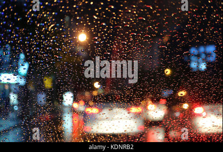 Blurred vehicles and tail lamps seen through the raindrops on car windshield at night Stock Photo
