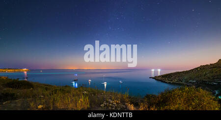 Long exposure of Mgiebah Bay in Malta on a clear summer night.  Street lights from Sicily can be clearly seen in the background on the horizon. Stock Photo