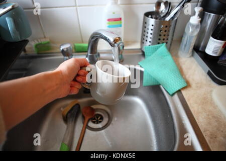 grey mug in metal washing up sink, with hand Stock Photo