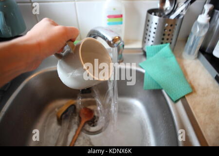 grey mug in metal washing up sink, with hand Stock Photo