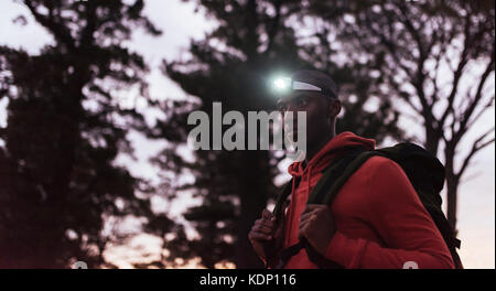 Young African man wearing a headlamp jogging at dusk Stock Photo