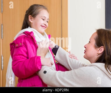 Family portrait of happy mother helping cheerful little girl to dress up on the doorway Stock Photo