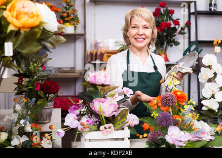 Cheerful woman florist in apron with tools in hands  in floral shop Stock Photo