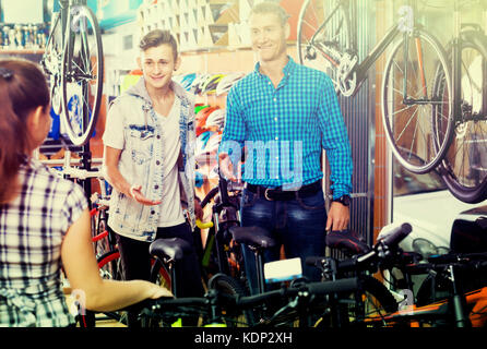 happy smiling father with teenage son getting help from female seller in bike store Stock Photo