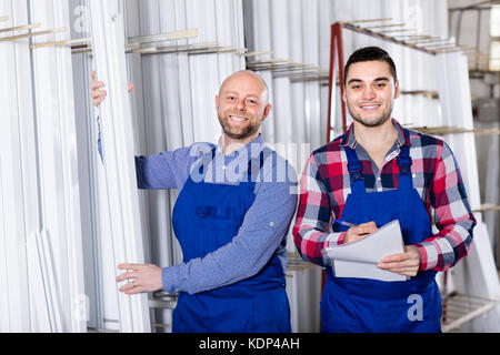 Two smiling production workers in coverall with different PVC window in store Stock Photo
