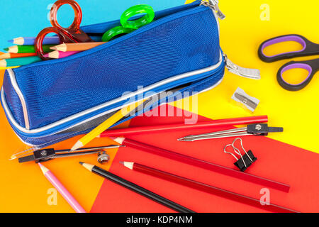 Blue pencil case full of colouring pencils and scissors on a colourful card background Stock Photo