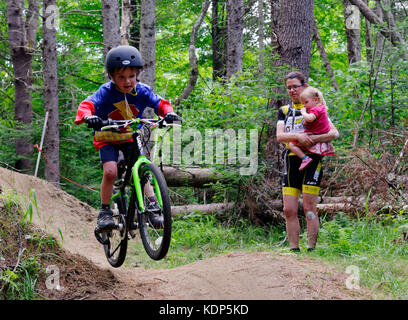 A young boy (5 yrs old) jumping in a mountain bike, while mum holding the sister, watches on Stock Photo