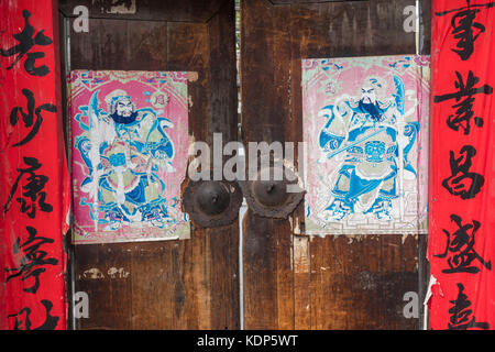 An old door with Spring Festival couplets, Chinese door-keepers and rusty knockers,  in a hutong. Beijing, China. Stock Photo