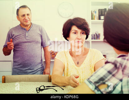 Serious retiree couple having conversation with adult daughter in home interior Stock Photo