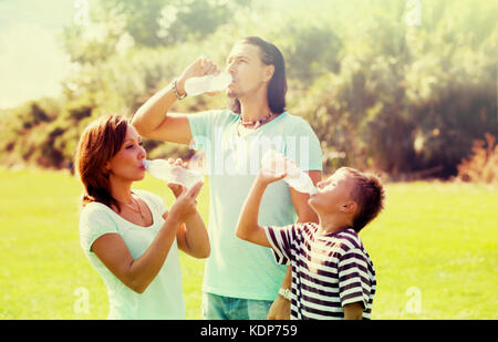 parents with teenager son drinking clean water from plastic bottles in summer park Stock Photo