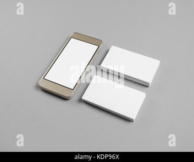 Smartphone with blank screen and two piles of business cards on gray paper background. Stock Photo
