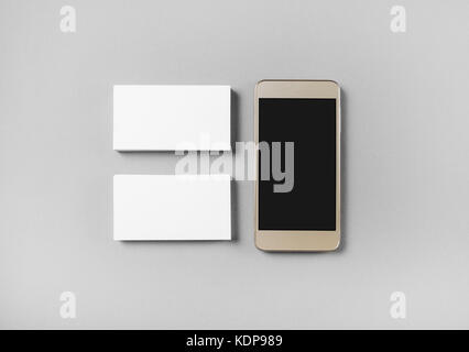 Two stacks of blank business cards and cellphone with blank screen on gray paper background. Top view. Stock Photo