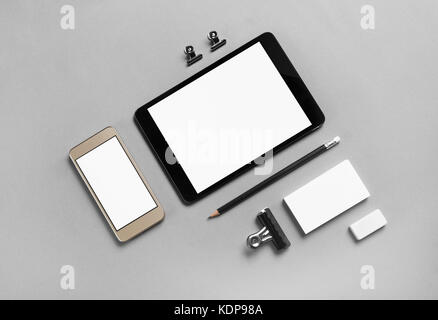 Gadgets with blank screens and stationery on gray paper background. Template for placing your design. Top view. Stock Photo