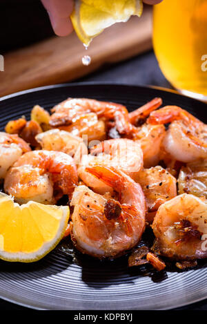 A hand squeezing lemon juice on roasted, grilled shrimp. Stock Photo