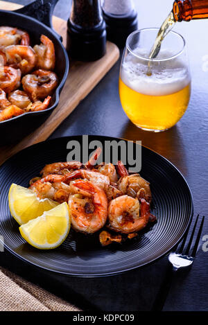 Skillet roasted jumbo shrimp on a black plate. Beer pouring into a glass. Stock Photo