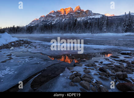 Winter Sunset at Castle Mountain, Banff National Park at -27 Celsius Degree with clear reflection in the ice water and foggy Bow river. Stock Photo