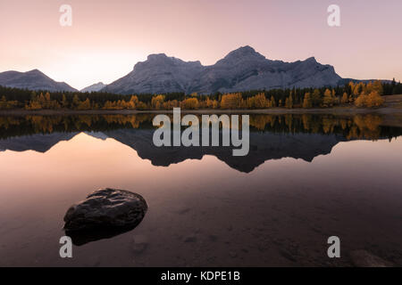 The sunset at Wedge pond in autumn, Kananaskis Country, Alberta, Canada.The trees are golden yellow and Mount Kidd was reflected in the lake. Stock Photo