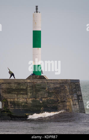 Aberystwyth  Wales UK, Sunday 15 October 2017  UK Weather: Practicing yoga by the lighthouse on a grey and overcast day in Aberystwyth, as the waves start to build in advance of the onslaught of the tail end of Hurricane Ophelia, which is scheduled to strike the west of the UK and Ireland overnight and into Monday. Despite losing much of its energy, the storm system  will bring damaging winds gusting up to 70 or 80mph in places, and the Irish Met office has issued a red warning   Photo © Keith Morris / Alamy Live News