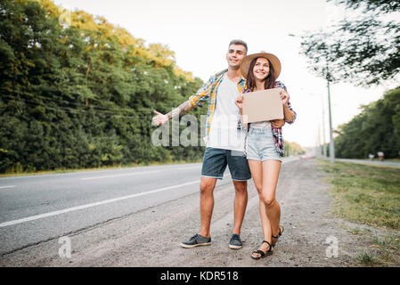 Young hitchhiking couple with empty cardboard. Hitchhike adventure of man and woman. Happy hitchhikers on road Stock Photo