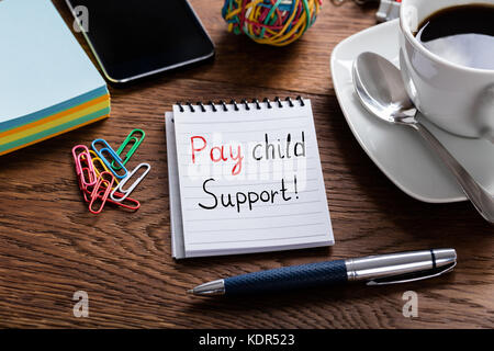 High Angle View Of Pay Child Support Concept Written On Notepad At Wooden Desk Stock Photo
