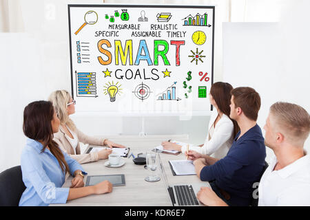 Group Of Businesspeople Looking At Smart Goals Concept On Projector Screen In Conference Room Stock Photo