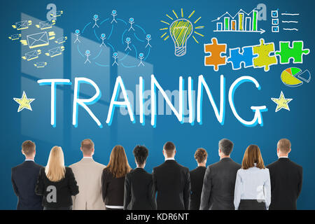 Rear View Of Businesspeople Looking At Training Concept Drawn On Blue Wall Stock Photo