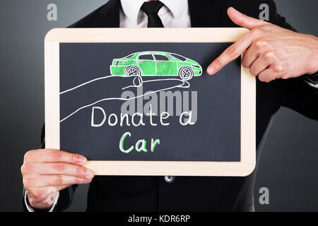 Close-up Of Businessman Showing Car Donation Concept On Slate At Grey Background Stock Photo