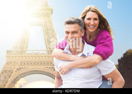 Portrait Of Happy Man Piggybacking His Wife Near Eiffel Tower Stock Photo