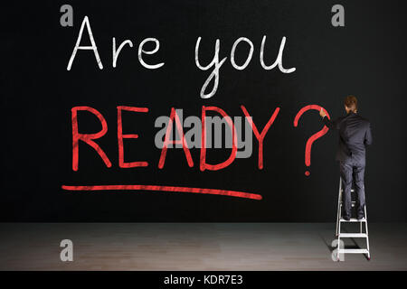 Rear View Of Businessman Standing On Staircase Writing Are You Ready Text On Blackboard Stock Photo