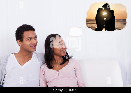 Young African Couple Sitting On Sofa Dreaming Of Spending Romantic Vacation With Each Other Stock Photo