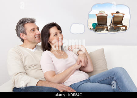 Matured Happy Couple Sitting On Sofa Dreaming Of Spending Vacation Together On Beach At Home Stock Photo
