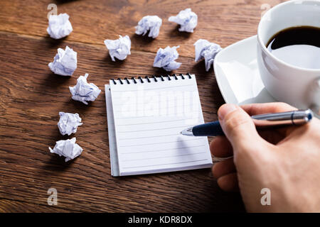 Close-up Of Businessperson Hand Holding Pencil On Blank Notebook Near Crumpled Paper On Wooden Desk Stock Photo