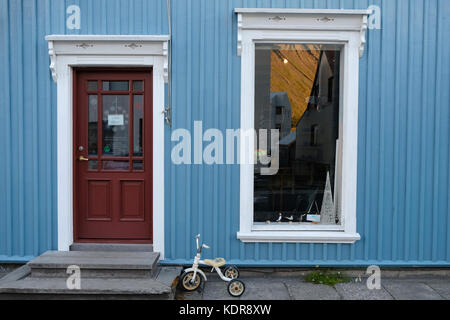 Traditional residential blue house with front door, window reflection and child's bicycle stands in Isafjordur, Westfjords, Iceland Stock Photo