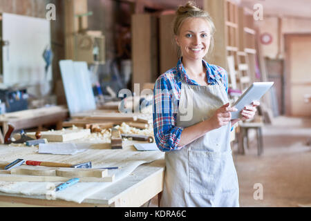 Young Carpenter Using Digital Tablet in Woodworks Shop Stock Photo
