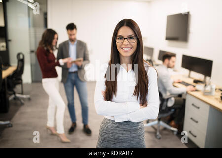 Businesswoman posing while other businesspeople talking in background Stock Photo