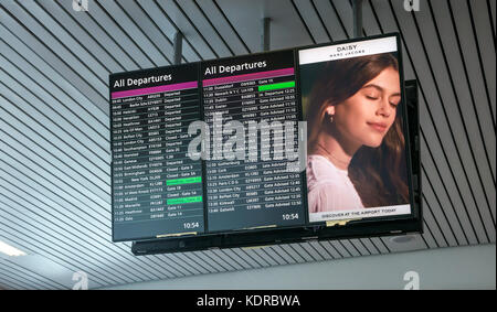 Departures of flights listed on electronic information board at Heathrow Terminal 5 with advert for Daisy perfume by Marc Jacobs Stock Photo