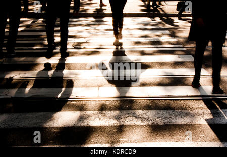 Blurry zebra crossing with silhouettes and shadows of people walking in the cold and sunny autumn in black and white Stock Photo