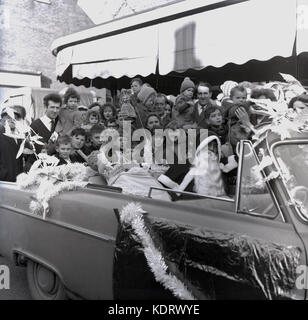 1960s, historical picture showing a group of excited young children and parents welcoming Father Christmas with his sack of gifts arriving in an open-top car, England, UK. Stock Photo