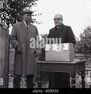 1960s, historical picture, two men, an elderly priest and a local  parishioner stand together outside with donation envelopes for the church's fund raising activities, England, UK. Stock Photo