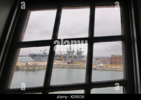 A view of the Royal Navy flagship HMS Queen Elizabeth through a window on Lord Nelson's flagship HMS Victory Stock Photo