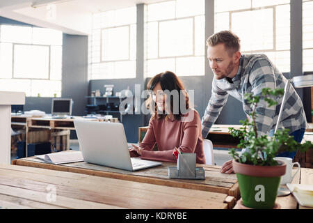 Smiling young colleagues using a laptop together in an office Stock Photo