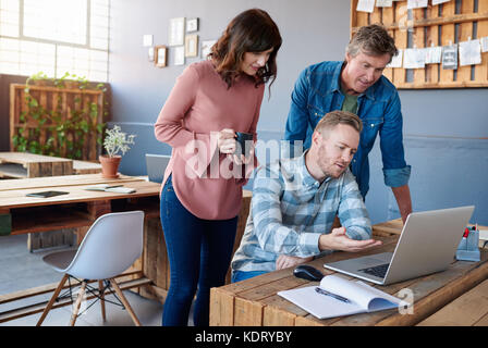 Focused young office colleagues using a laptop together  Stock Photo